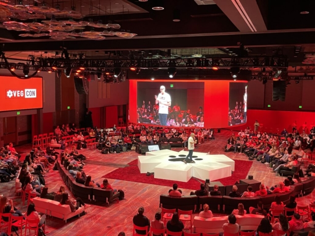 CEO Speaks from central stage, shaped in a medical icon with a logo in the middle. Overhead a 360 degree screen and audience all around watching in.